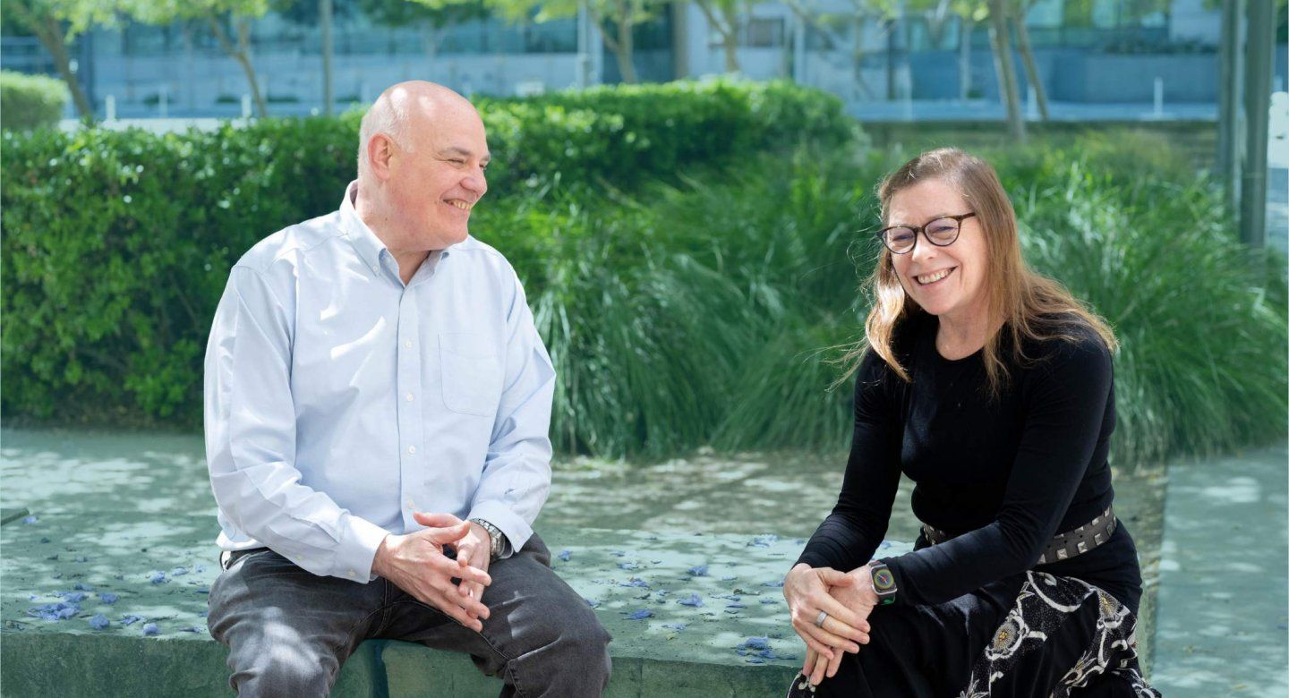 Hellman and Neilands sit in outdoor courtyard smiling.