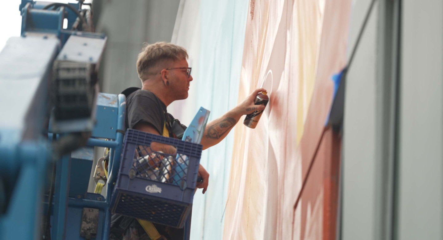 Muralist paints multi-color art on building.