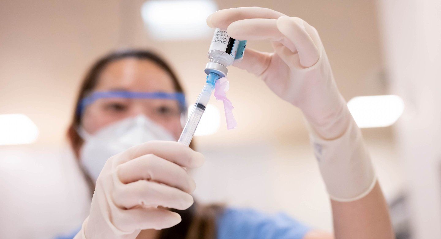 Nurse wears gloves and moves covid vaccine into syringe.