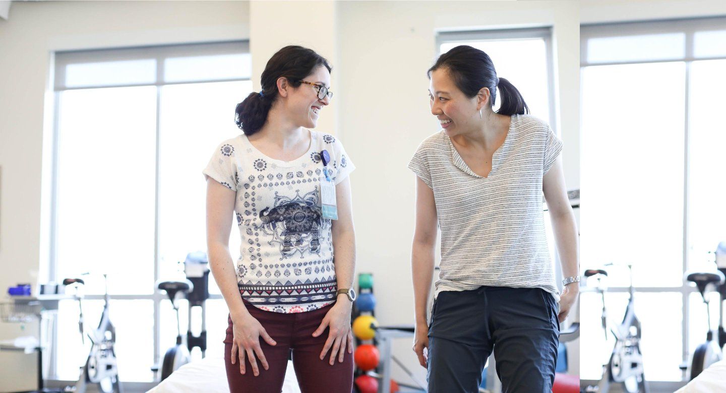 Two women smile at the gym and look at eachother.