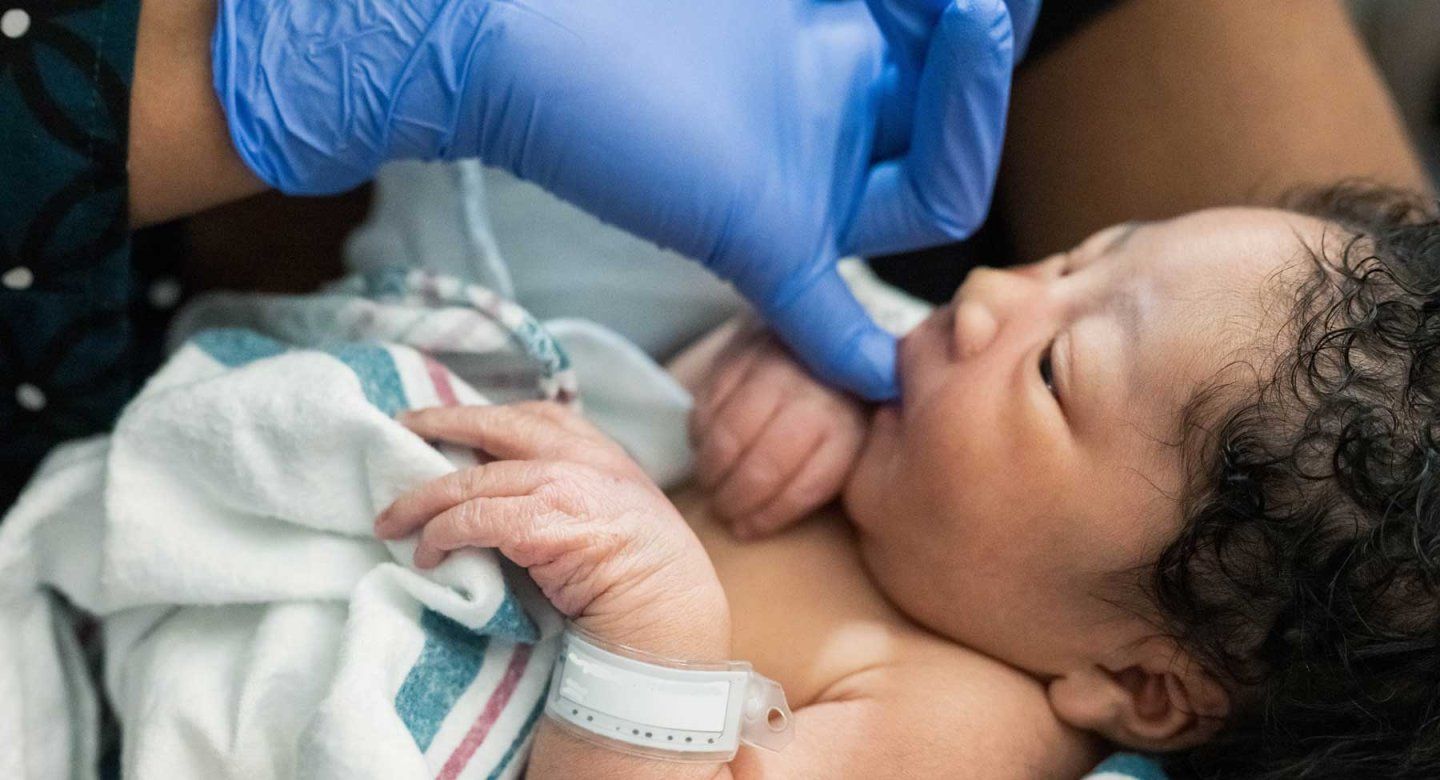 A nurse wearing a blue latex glove holds a newborn baby boy.