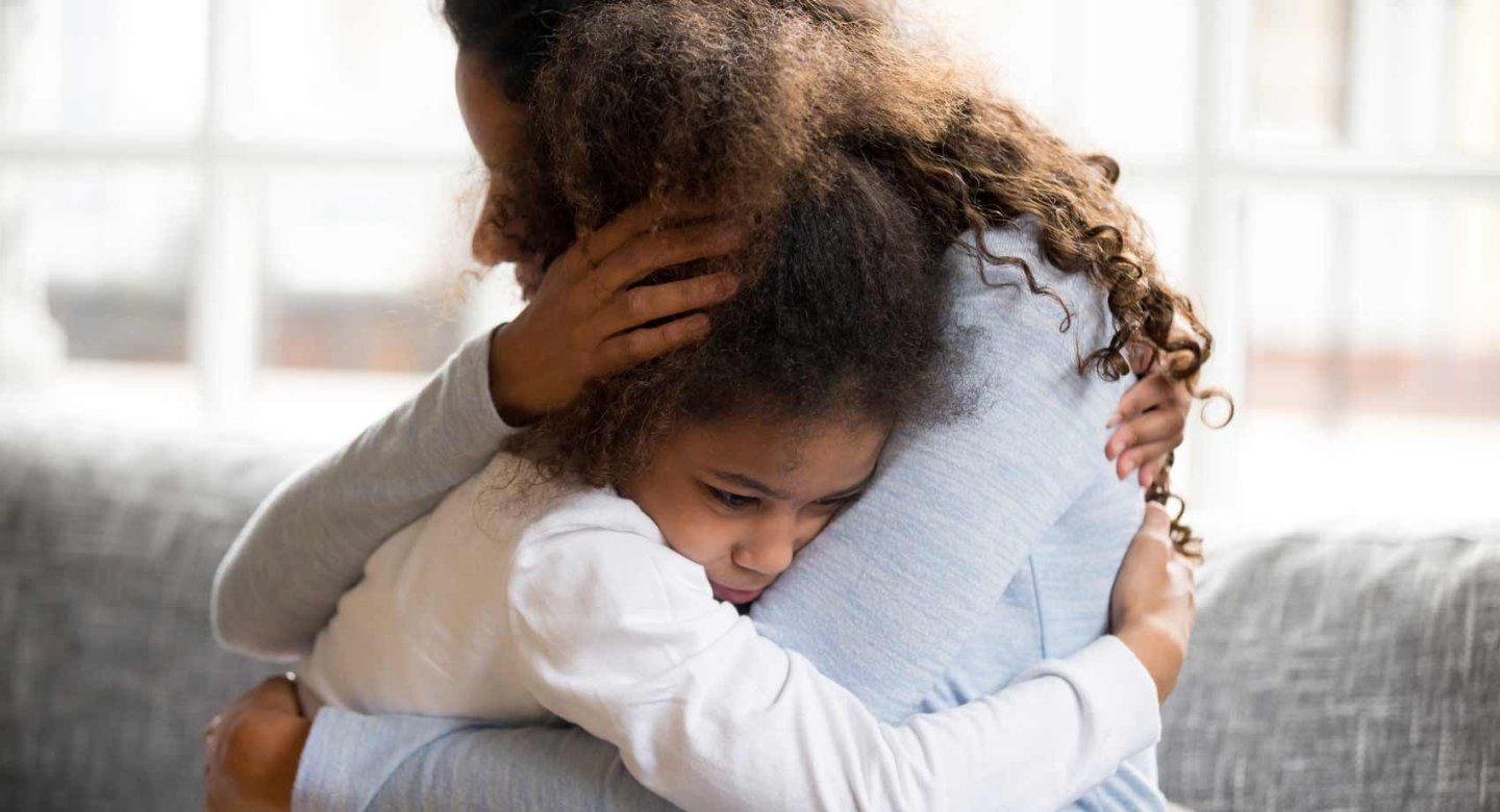 A mother holds her young daughter who shows signs of stress.