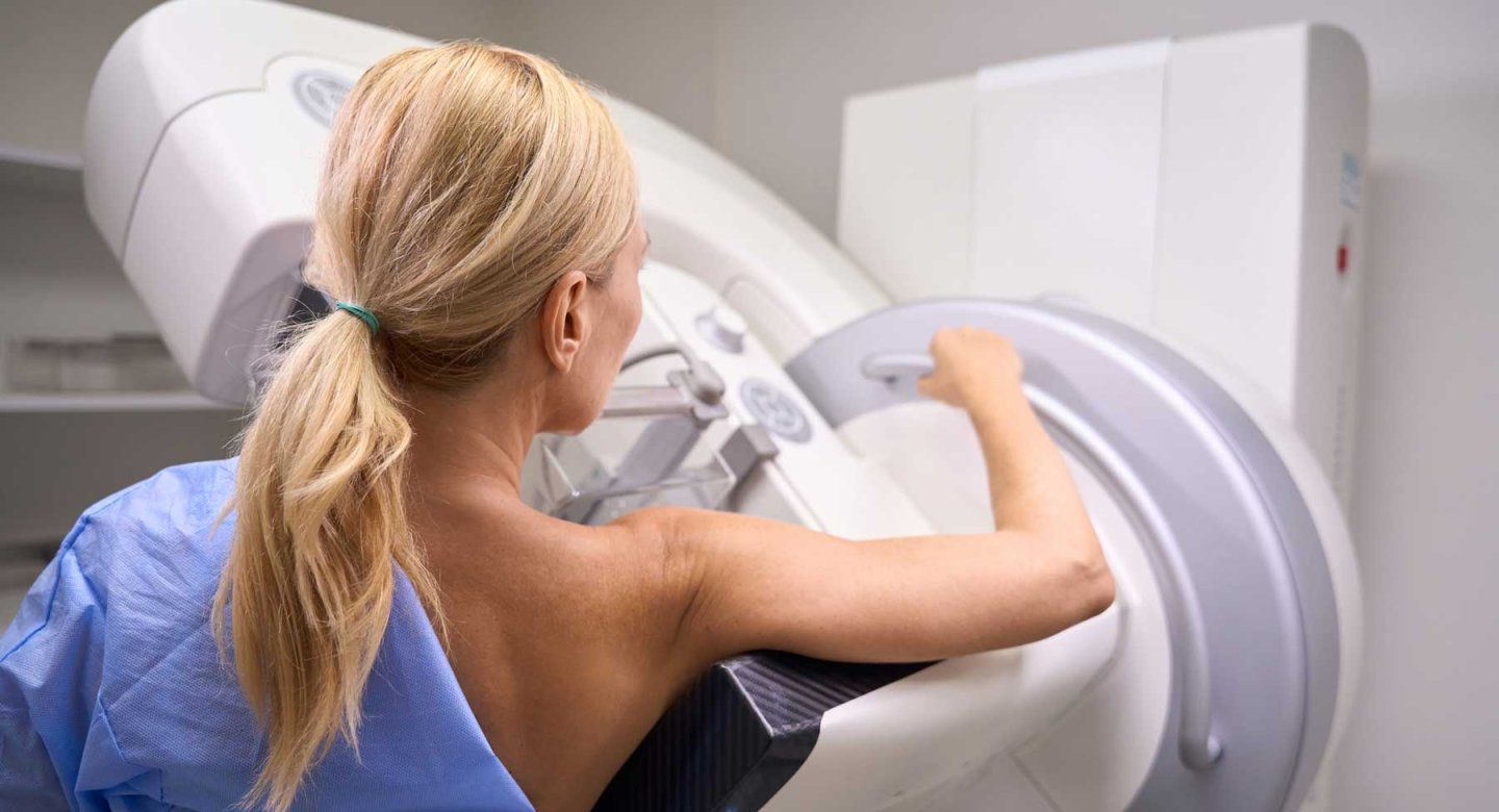 A woman stands at a mammogram machine.