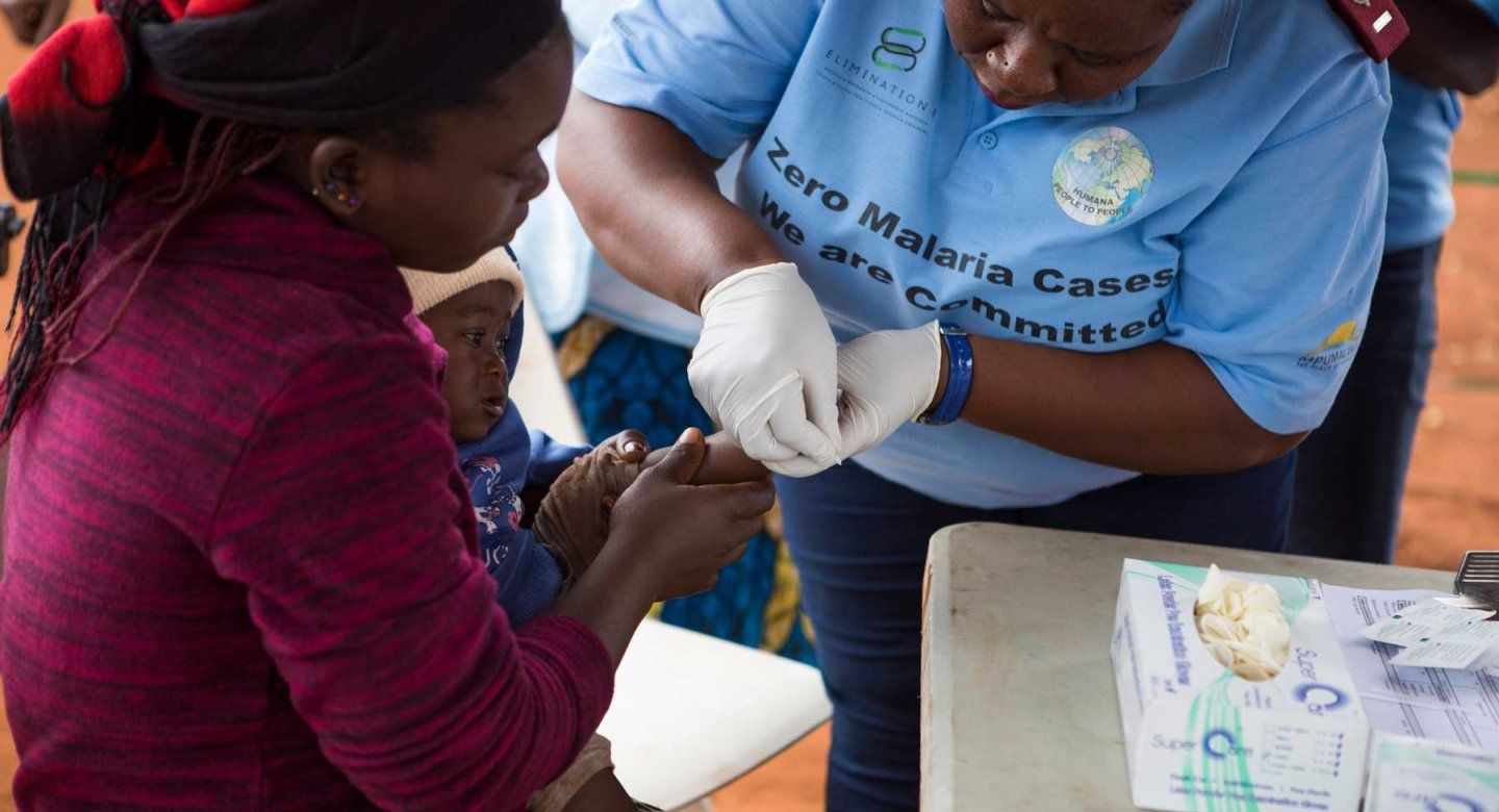 A mother holds her baby as a medical practicioner delivers a malaria vaccine.