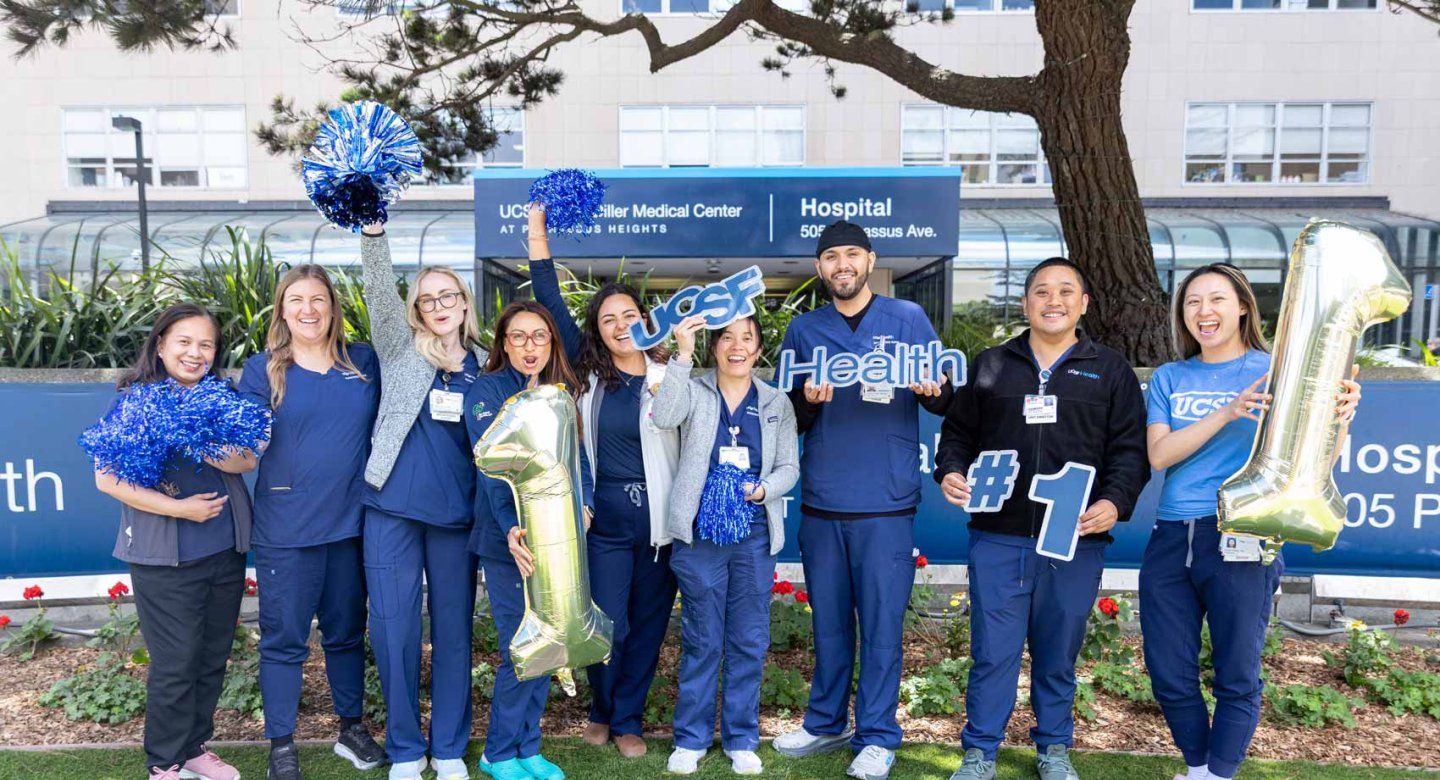 Medical professionals wearing medical scrubs cheer and hold balloons and pom poms outisde of the U C S F Medical Center at Parnassus Heights.