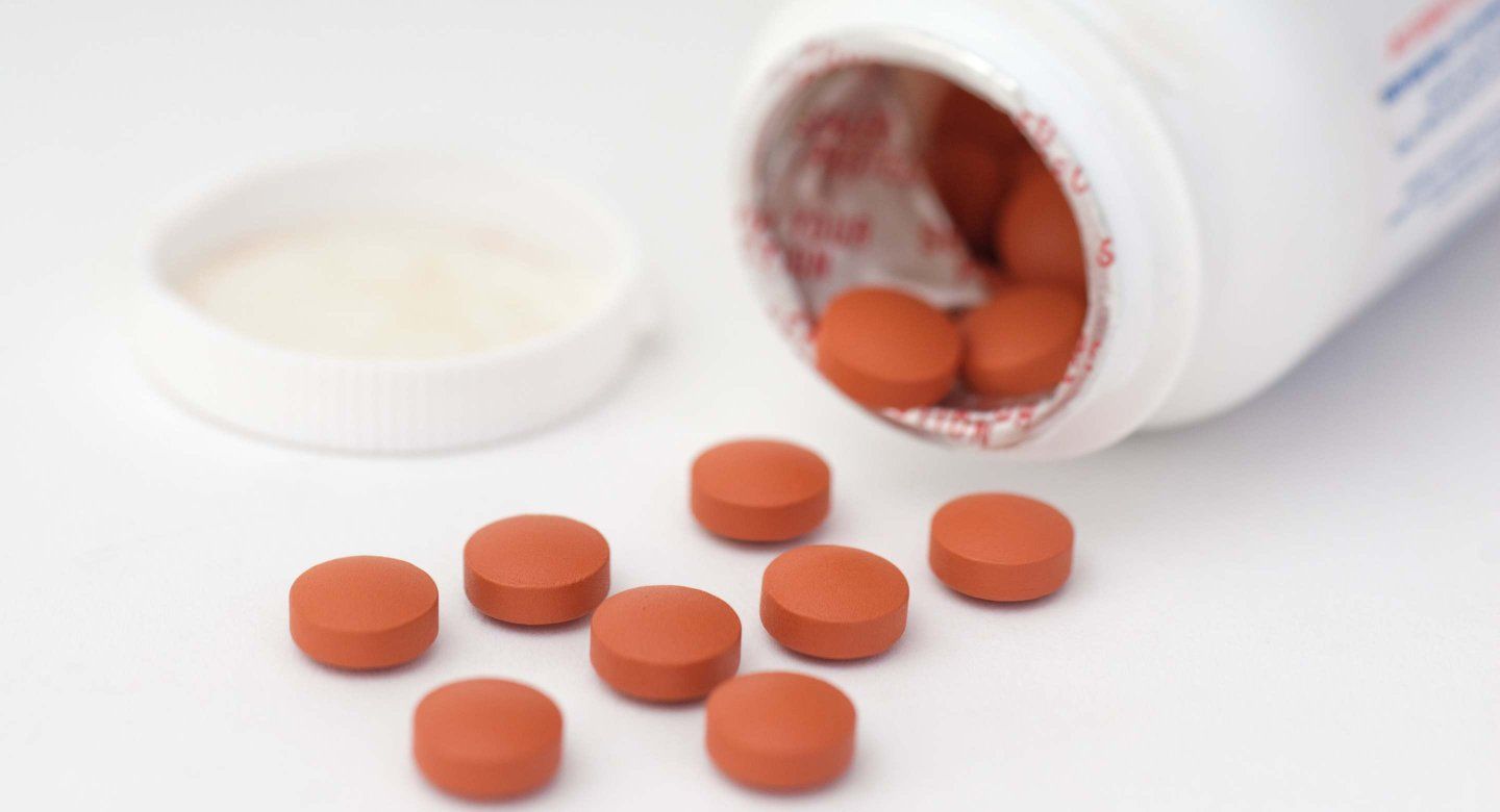 Close-up of a white prescription pill bottle with a blue and white capsule resting on the label and other pills scattered in the background.