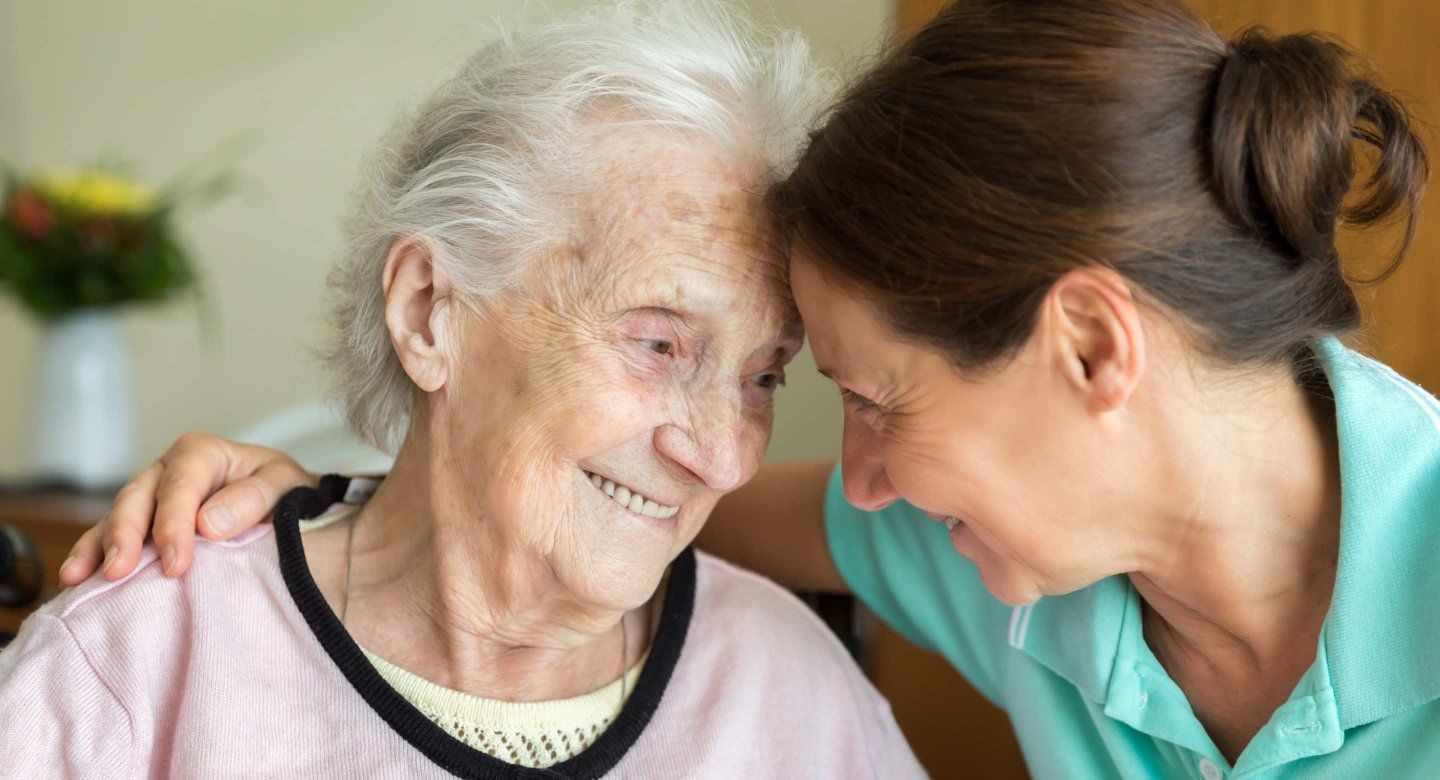 An older woman smiling warmly while interacting closely with another person outdoors.