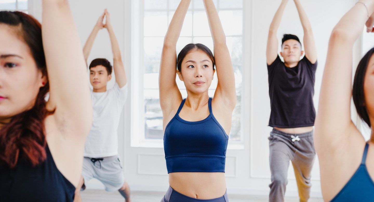 Five people in yoga class, standing and stretching their arms
