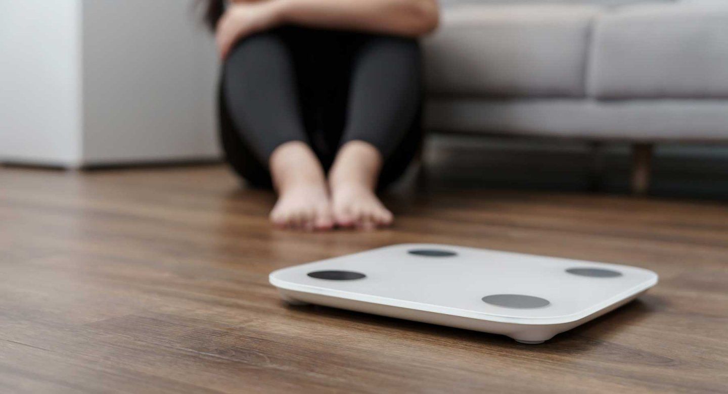A depressed woman sits in front of a scale.