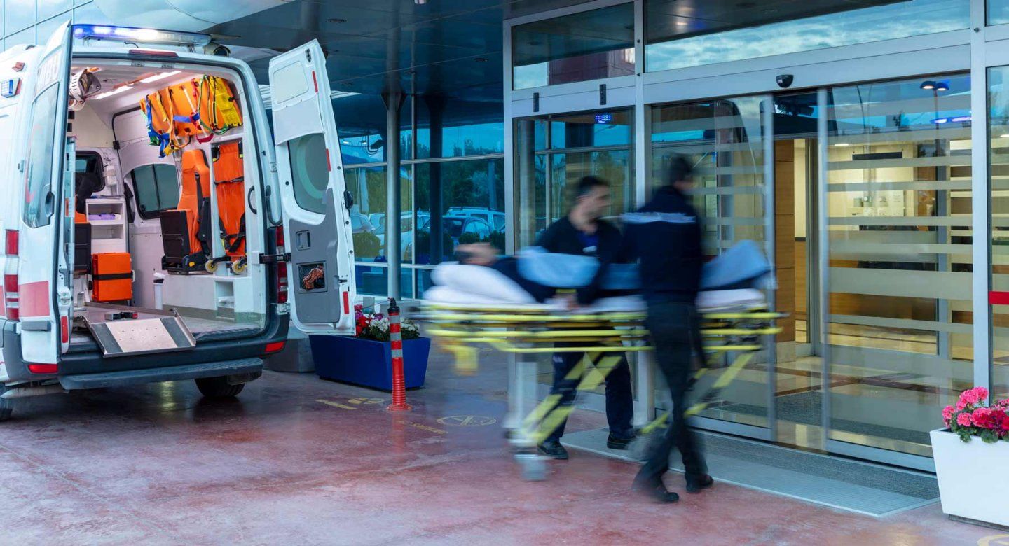Paramedics rush in to carry a person on a stretcher from an ambulance into an emergency department.