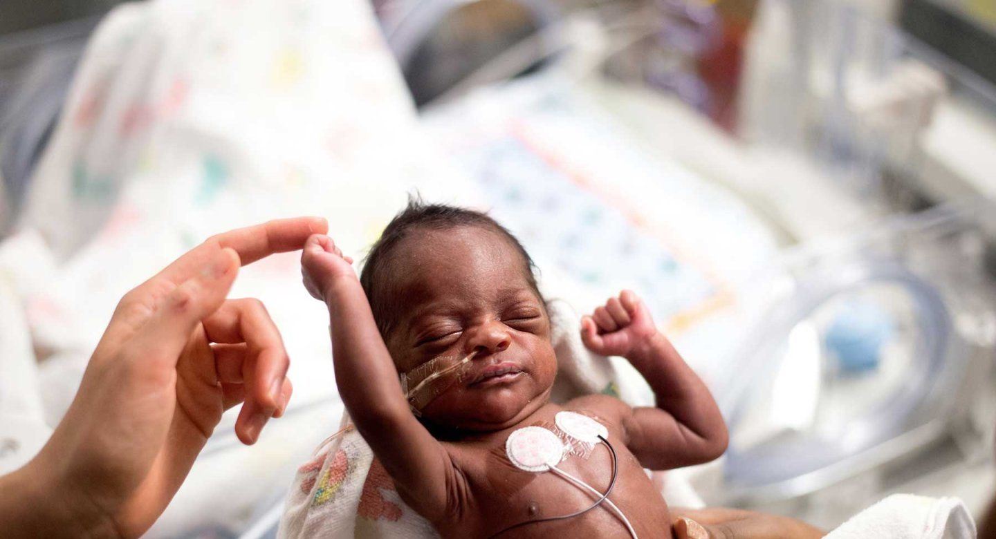 A preterm baby stretches his arm and touches a caretaker's finger.