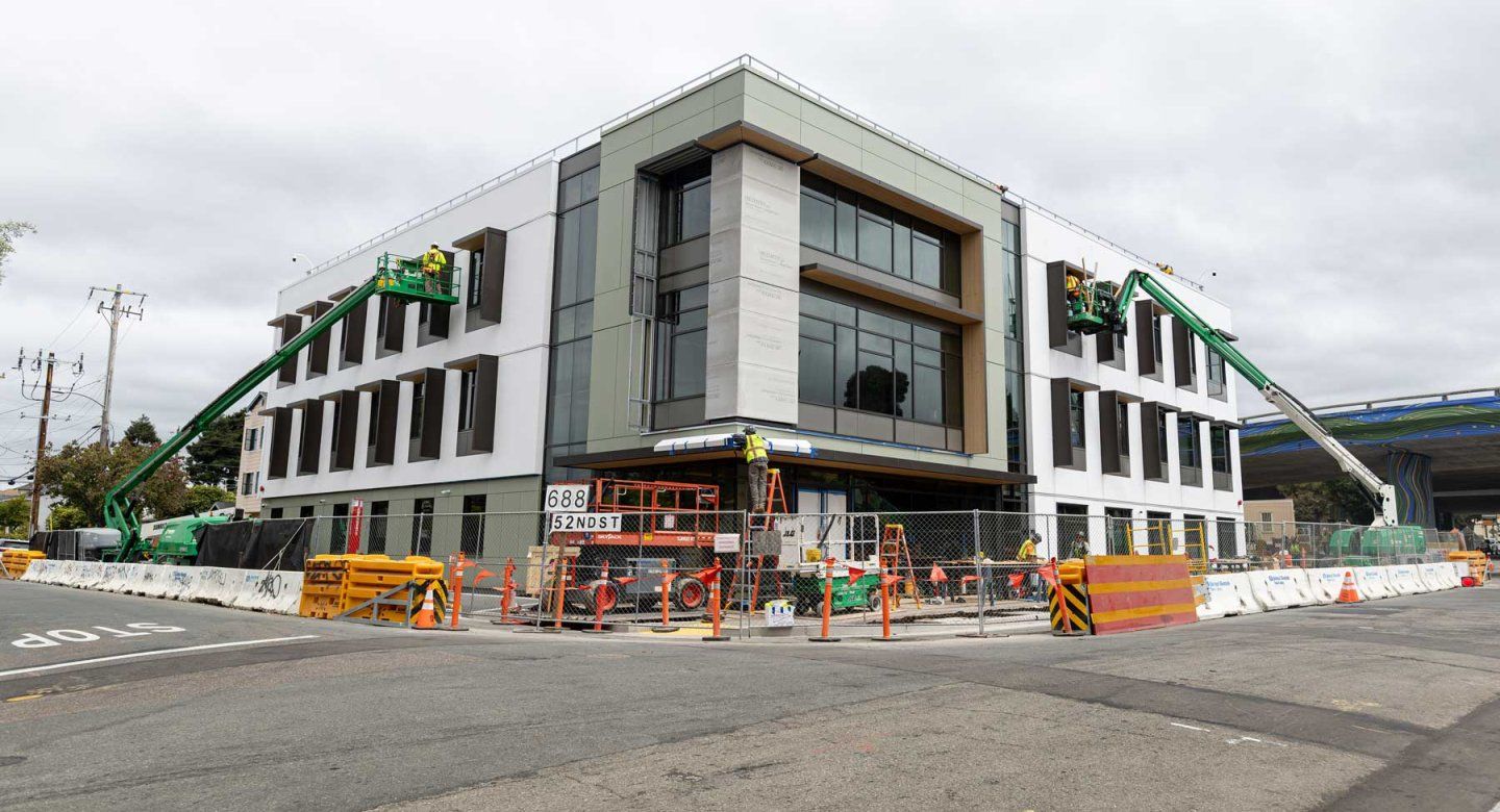 An exterior shot of construction of Temescal Hall with construction workers on cranes.