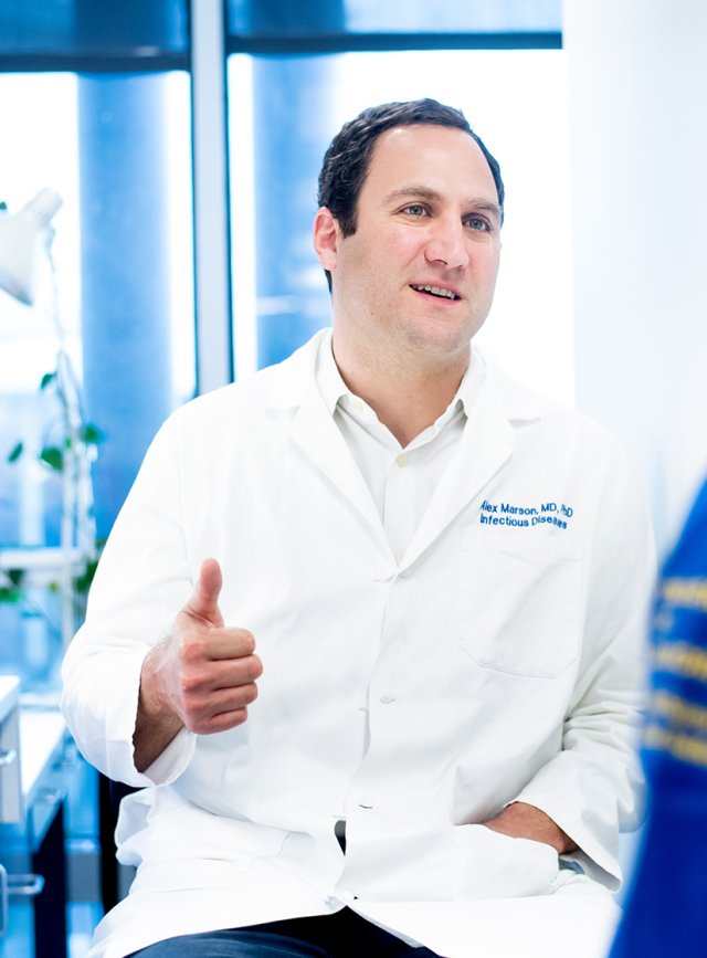 Alex Marson wearing a white coat in his lab and talking to a fellow researcher