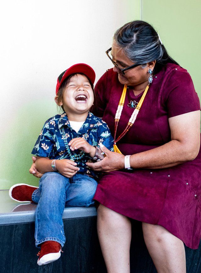 Un ragazzo di discendenza navajo sorride mentre viene abbracciato da sua nonna, anch'essa di discendenza navajo.