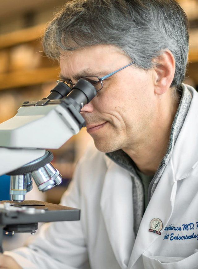 A male scientist wearing a lab coat looks into a microscope
