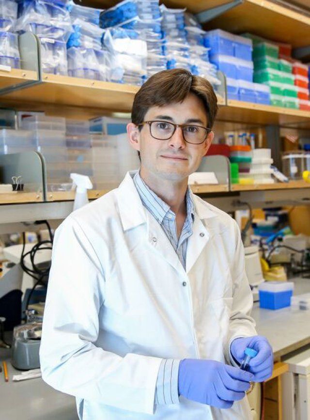 Matthew Spitzer wears a white lab coag and blue latex gloves as he stands in his lab at UCSF.