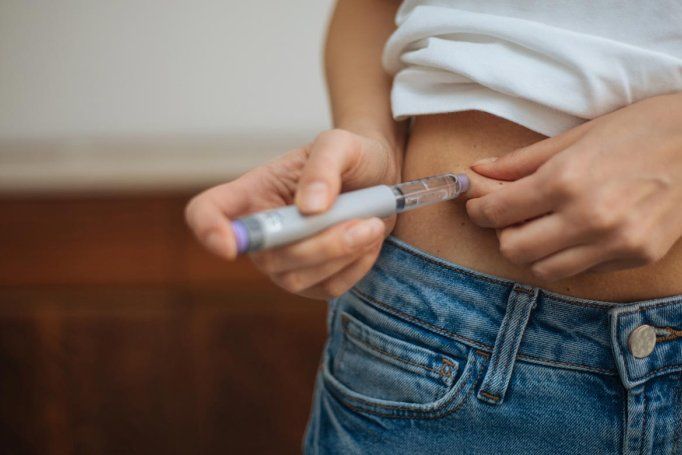 A woman lifts her shirt to inject a weight loss drug into her abdomen.