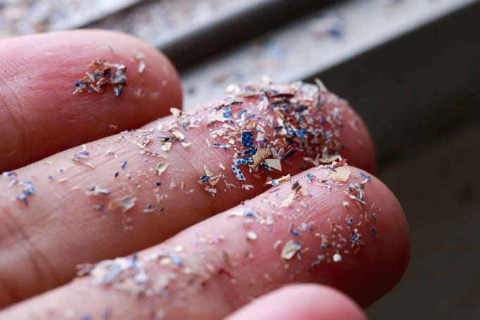 Fingers holding small pieces of microplastics.