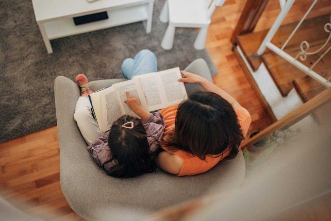 A child and mother read together on a couch.