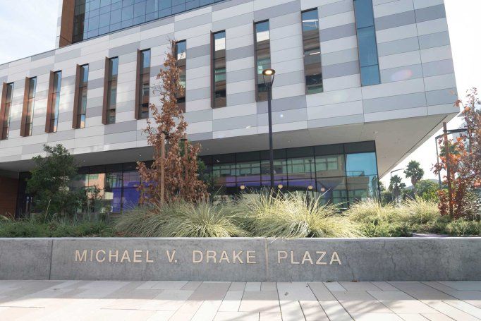 A low concrete wall in an outdoor plaza with embedded letters that read "Michael V. Drake Plaza."