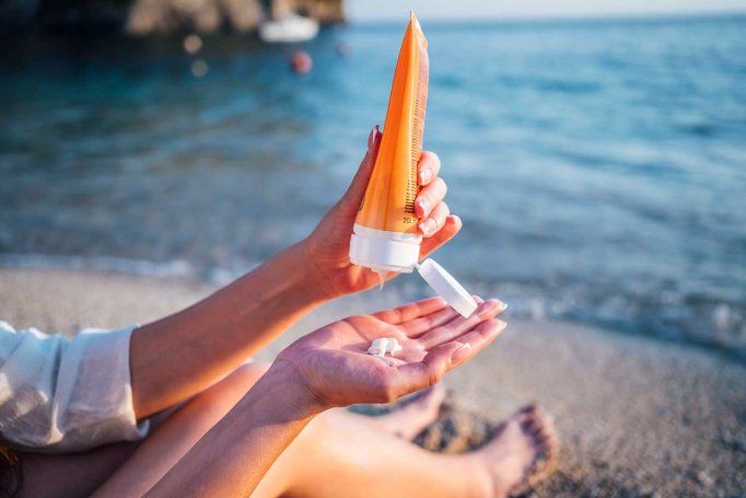 A woman applies sunscreen while sitting on a beach.