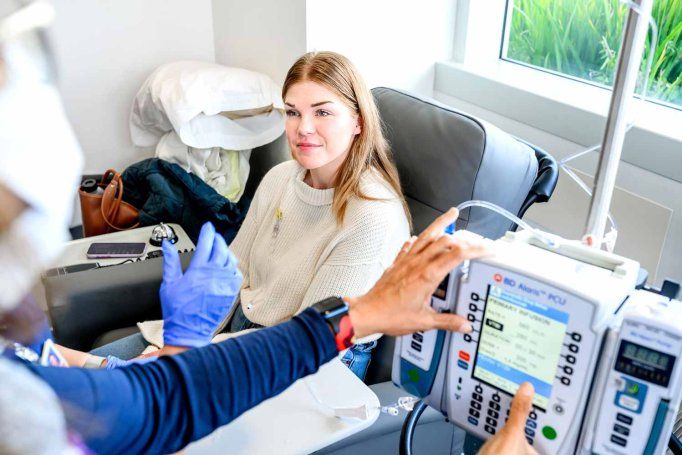 A young 30-year-old patient named Megan smiles as she is assisted by a medical professional while receiving an infusion to treat colorectal cancer.