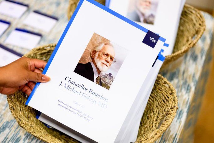 A woman's hand picks up a printed program for J. Michael Bishop's memorial.