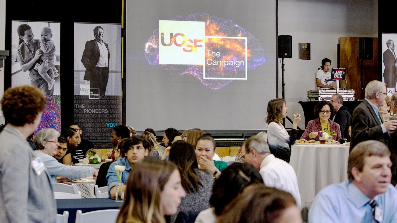 people eat in a room with a screen that says UCSF: The Campaign behind them