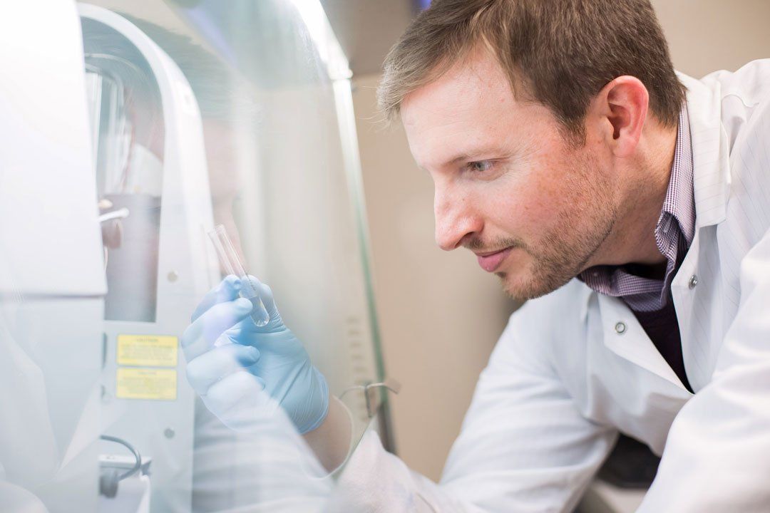 UCSF professor Kole Roybal examines a vial of liquid in his gloved hand
