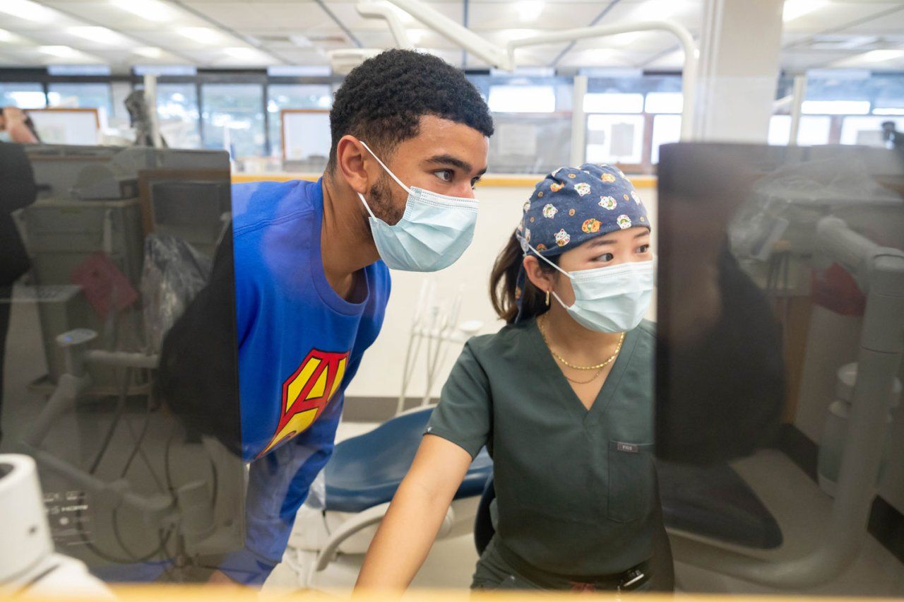 Two dental students look at a computer screen with dental records
