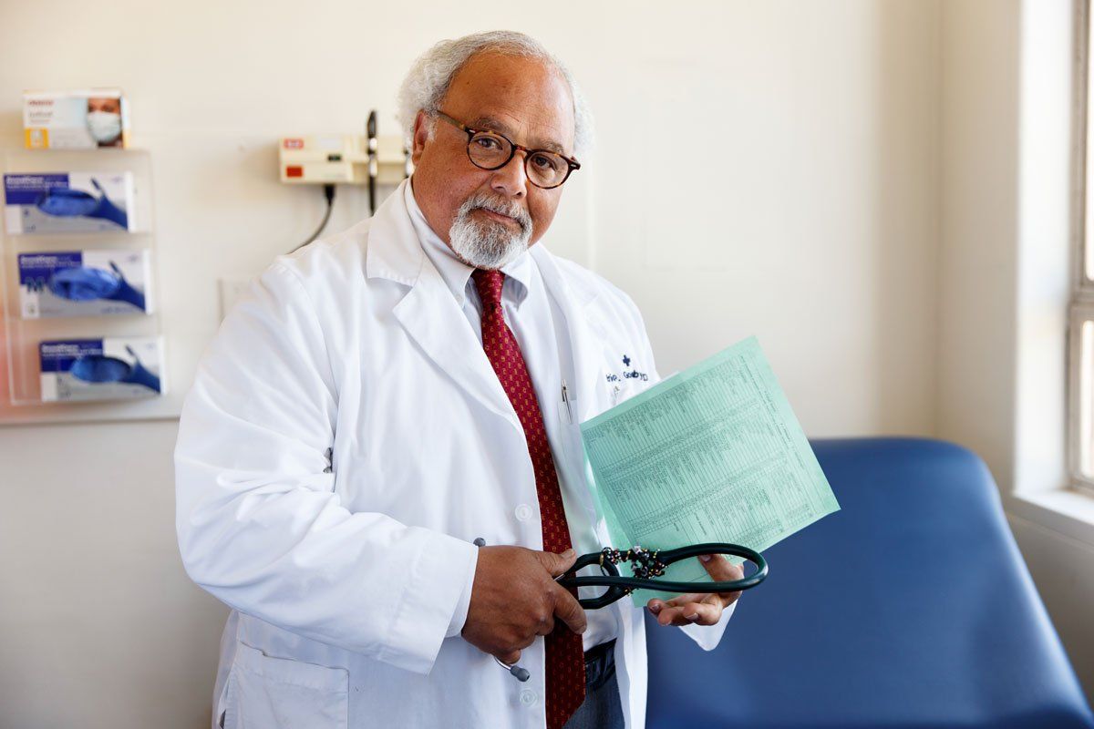Eric Goosby stands in an exam room holding a green document and a stethoscope