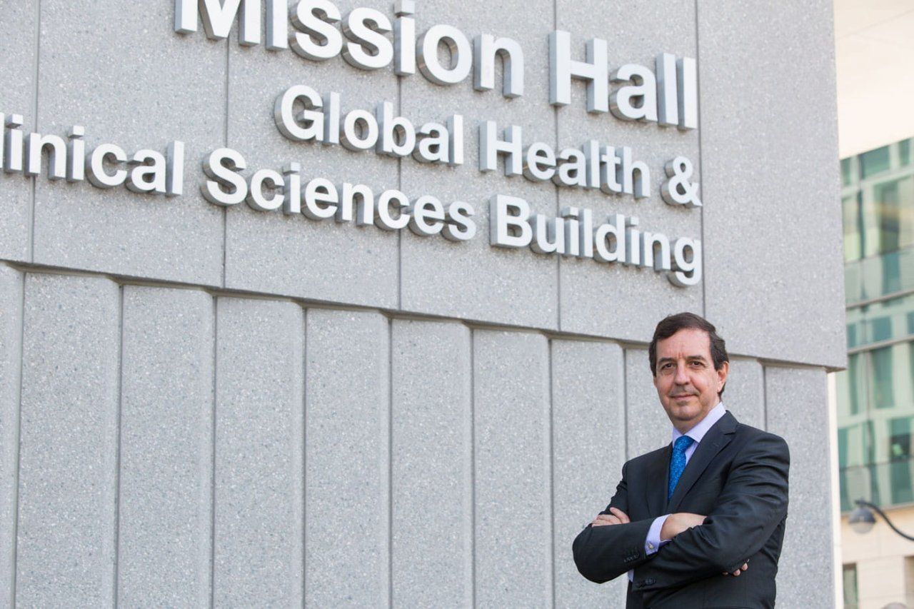 Jaime Sepulveda stands in front of Mission Hall. On the wall is signage reading "Mission Hall - Global Health & Clinical Sciences Building"