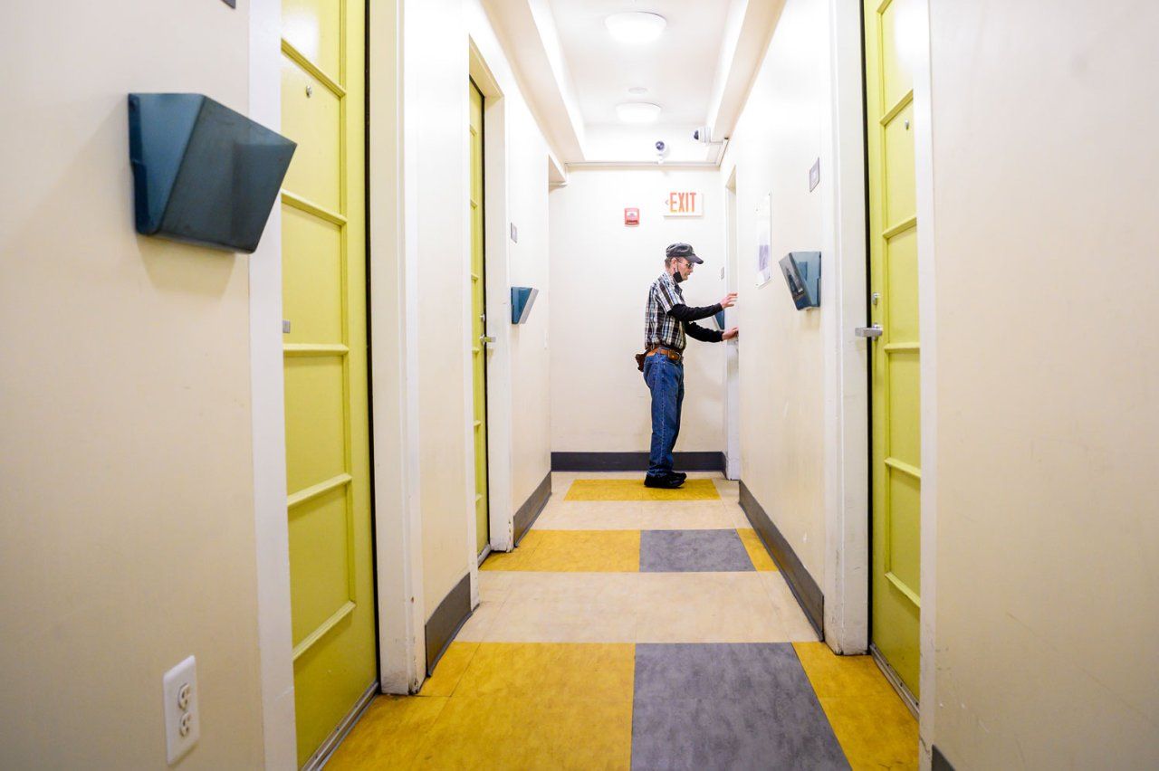 A man opens a lime green door at the end of a hotel hallway.