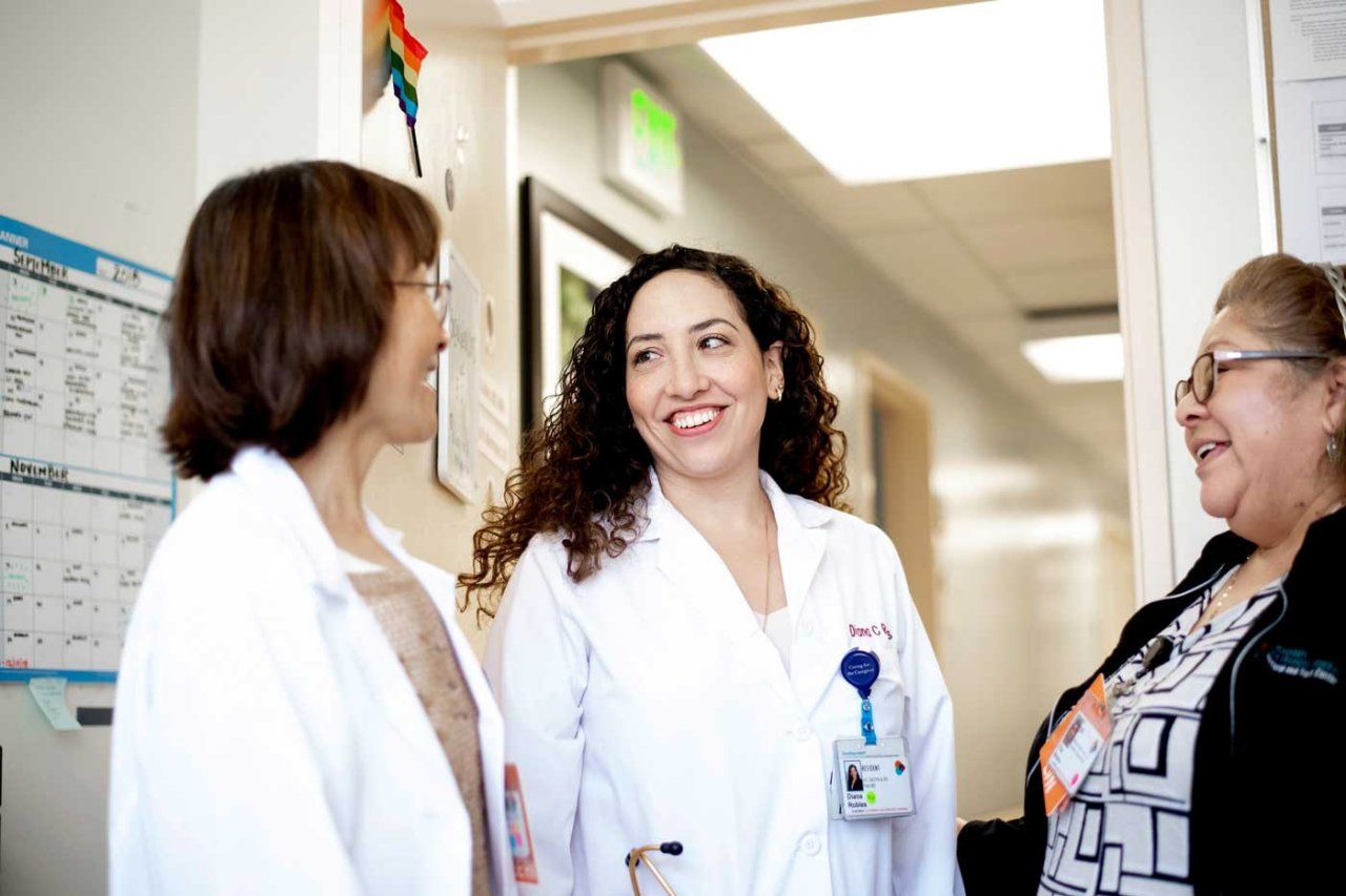 A female doctor wearing a white coat speaks with two nurses.