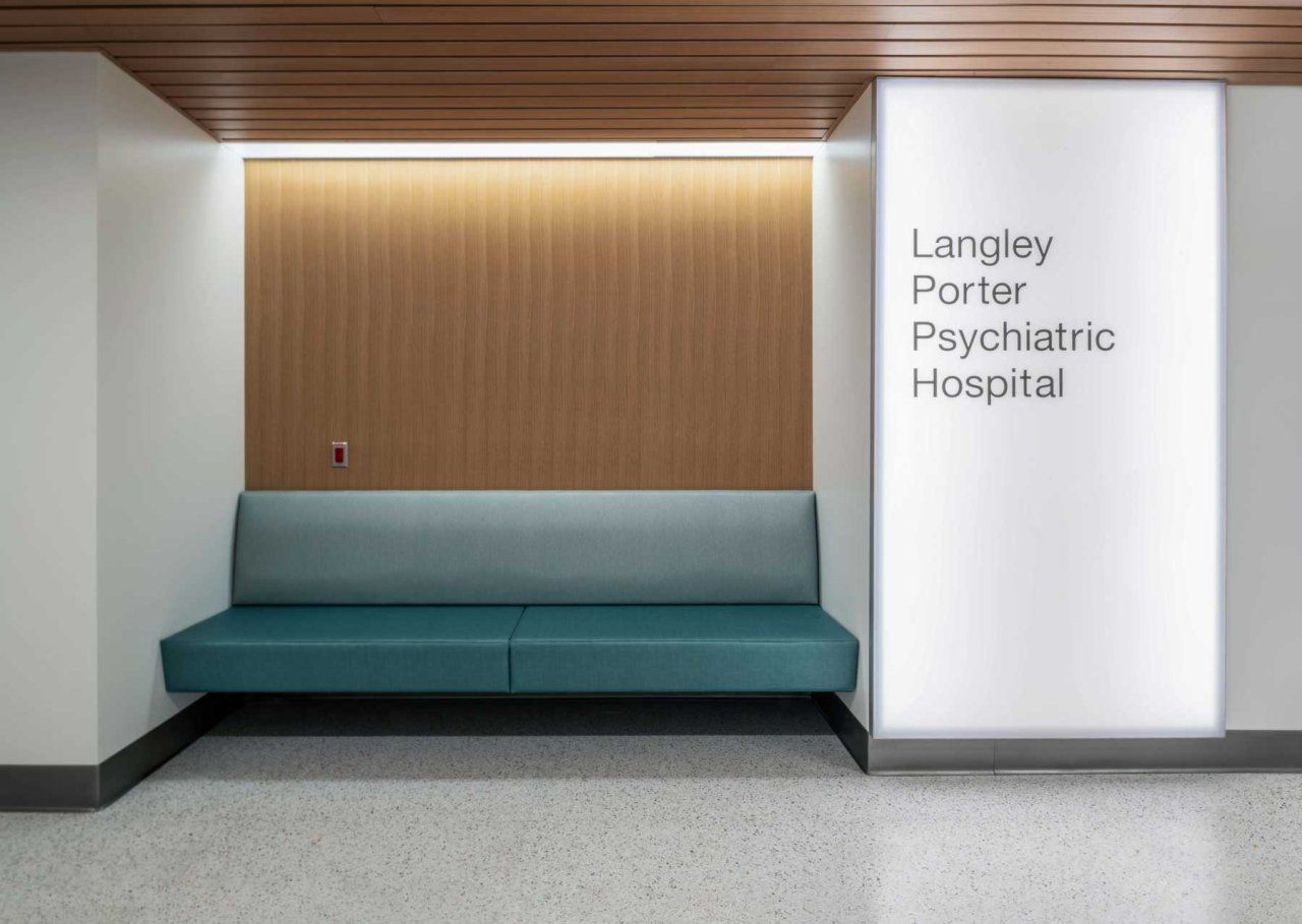 The entrance to the Langley Porter Psychiatric Hospital. A blue bench rests against a wood-panelled wall, and a light pillar reads "Langley Porter Psychiatric Hospital."