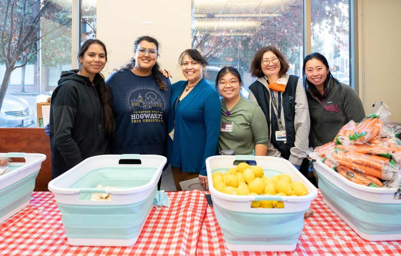 A group of women volunteers at a table with bins of fruit to give out to UCSF patients.