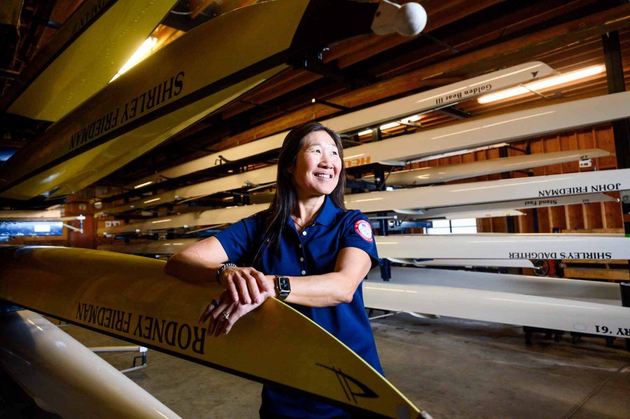 Cindy Chang smiles as she stands among multiple rowing boats.