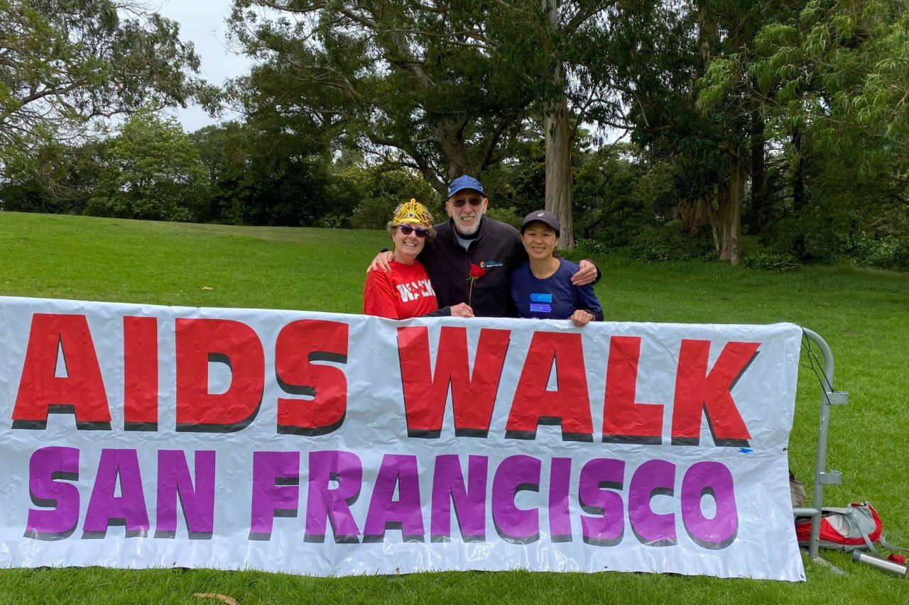 Three people standing behind an AIDS Walk San Francisco banner