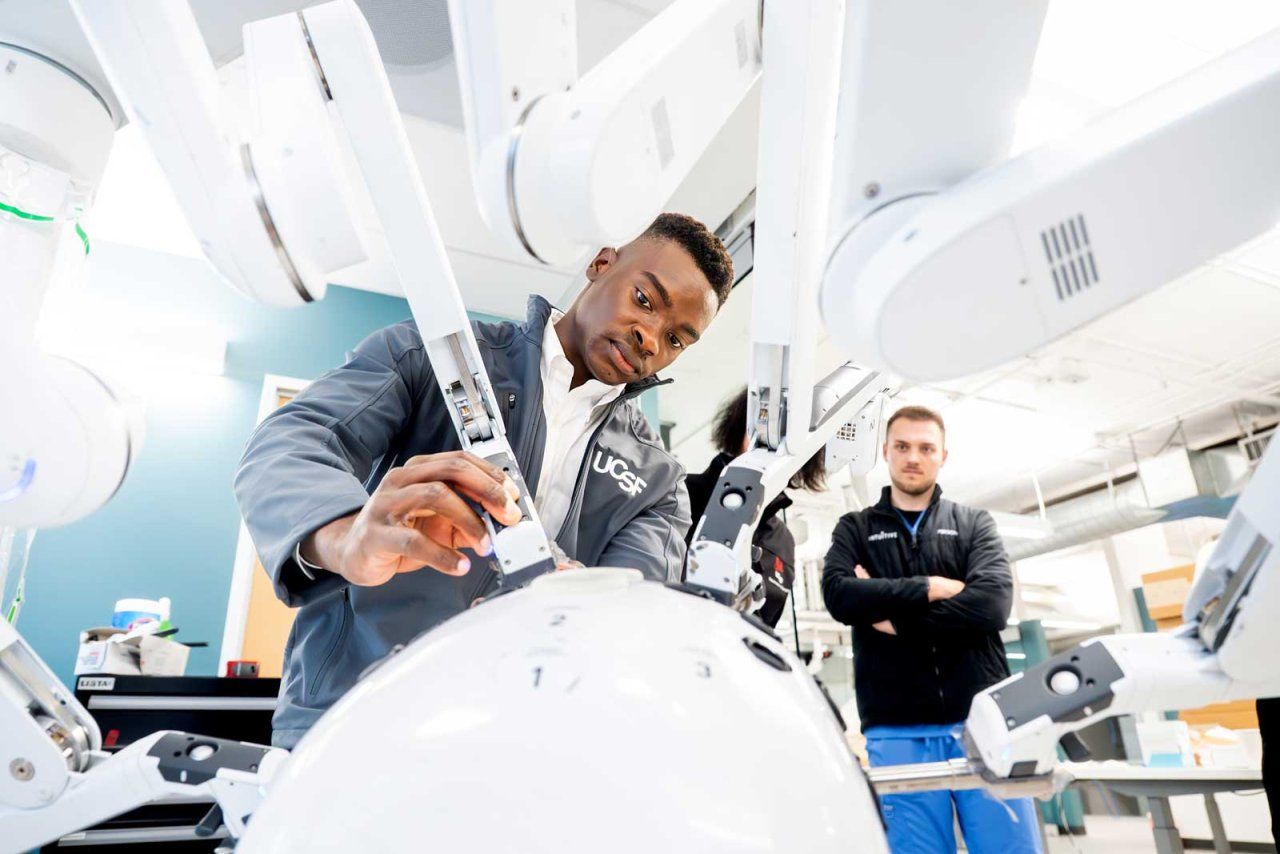 An intern works with the arms of a surgical robot with instructors watching on.