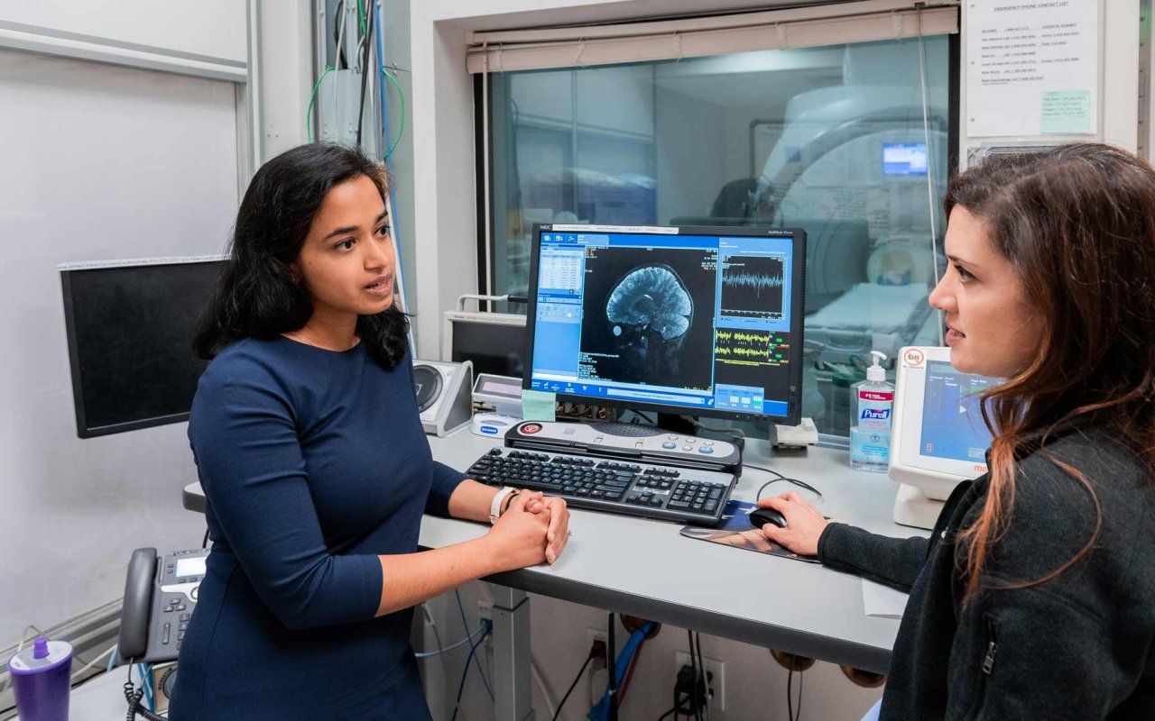 Two doctors speak in front of a computer monitor that shows a brain scan.