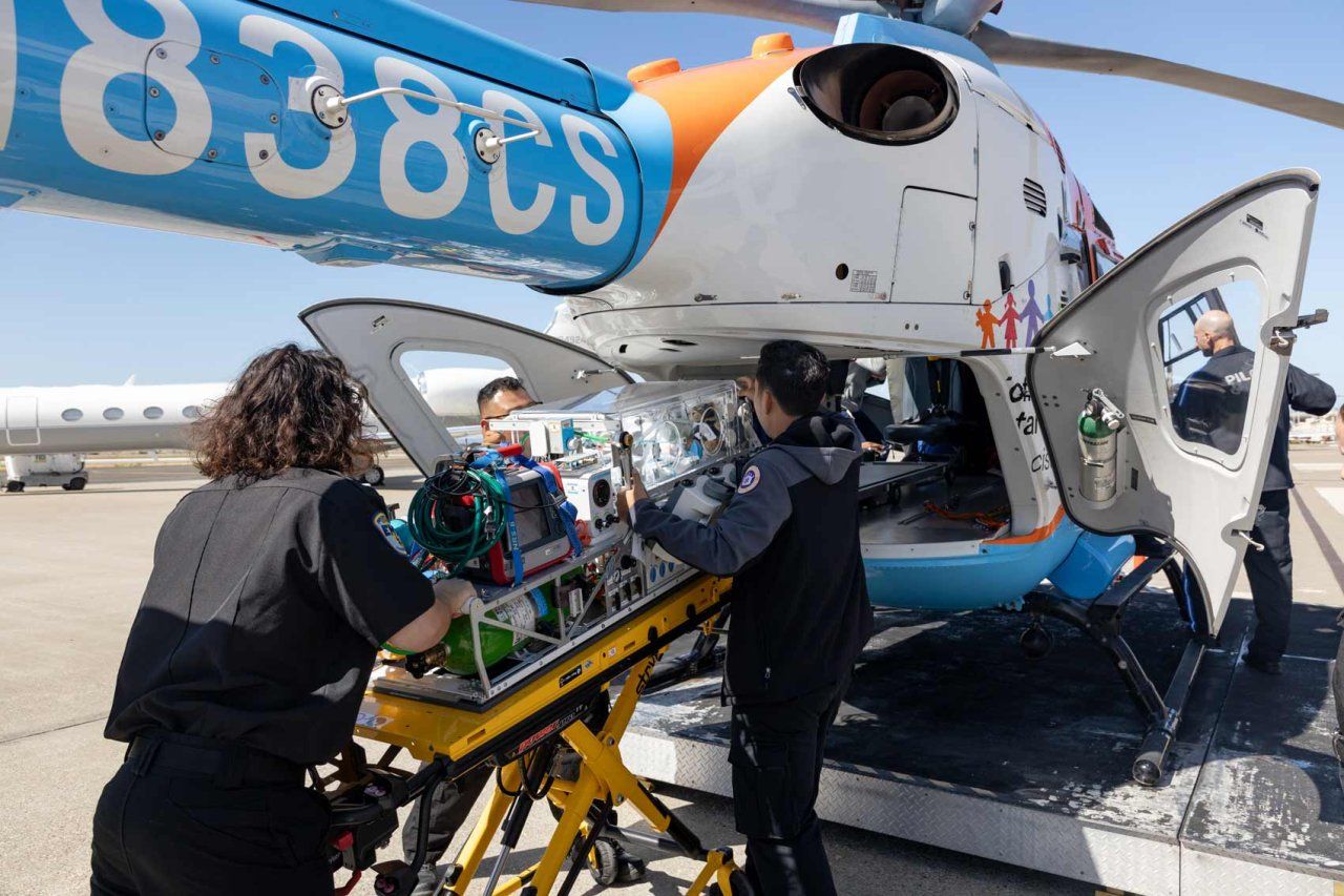 A group of emergency medical professionals load an incubator onto a U C S F Benioff Children's Hospitals helicopter for emergency transportation.