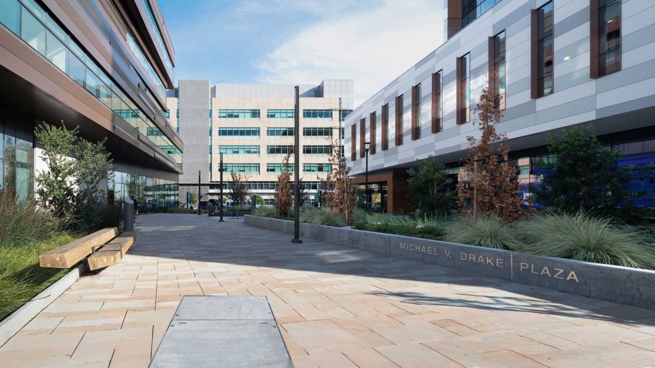 A low concrete wall in an outdoor plaza between two medical buildings with embedded letters that read "Michael V. Drake Plaza."
