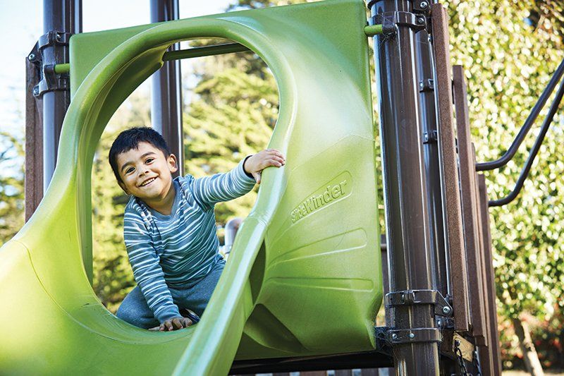 Steven Mendoza smiles at the camera before going down a slide on the playground