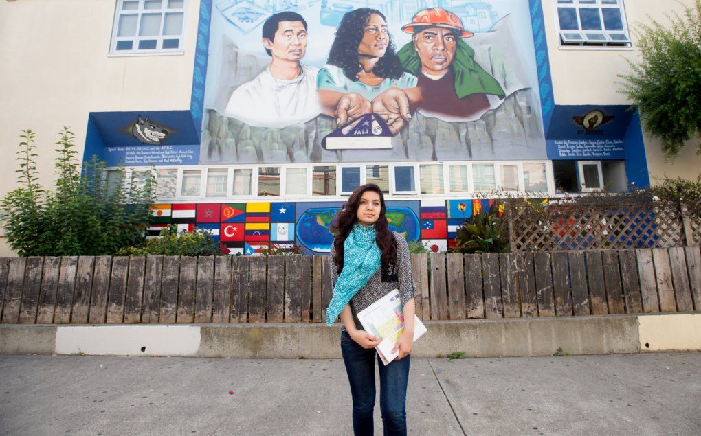 An SEP intern stands in front of a San Francisco high school with a multi-cultural mural