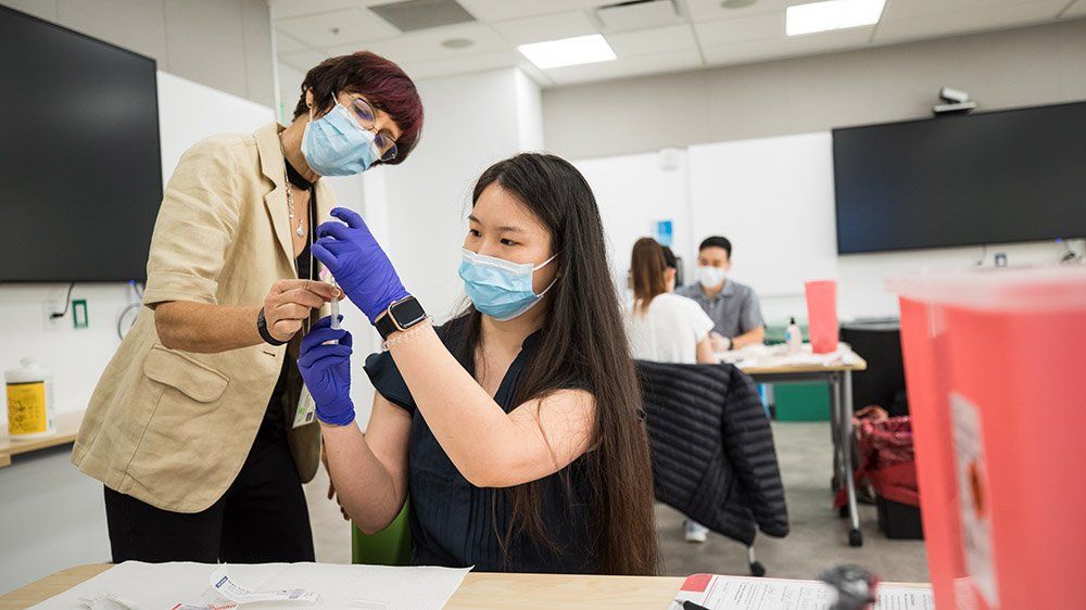 a teacher and student wear masks and gloves as they practice medical skills