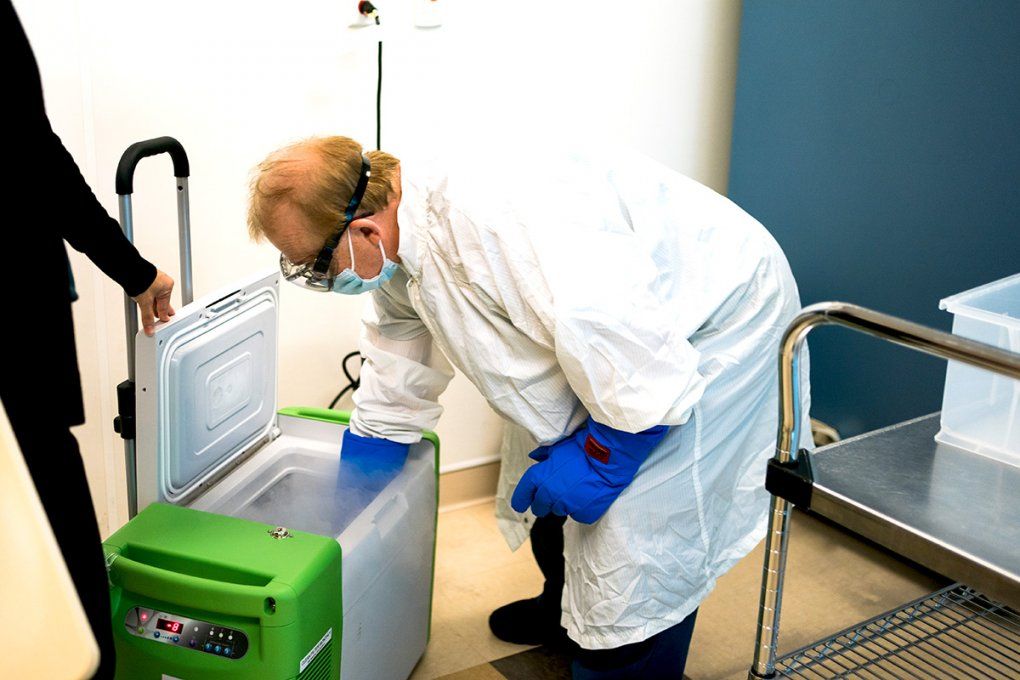A medical worker reaches into a refrigerated case emitting foggy air
