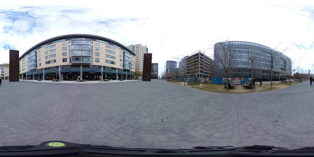 A broad bricked path leading through campus lined by shops and two large monoliths