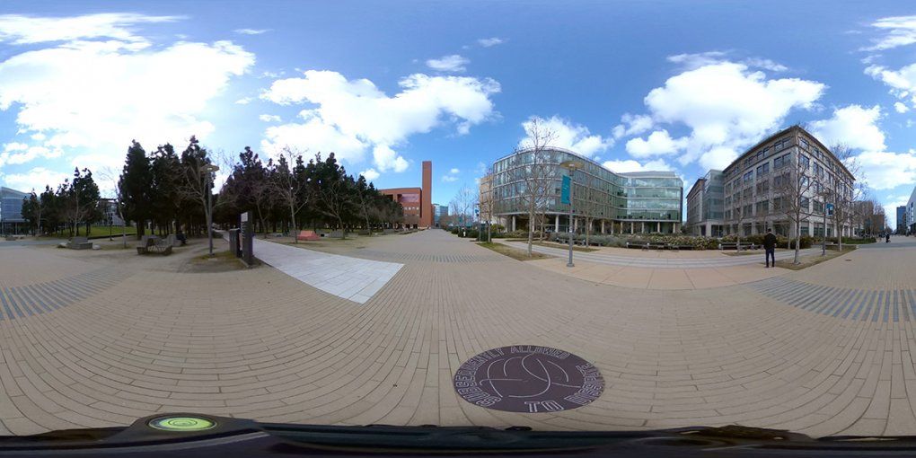 Multiple wide brick pathways lead around the edge and through Koret Quad with trees and benches before the surrounding buildings