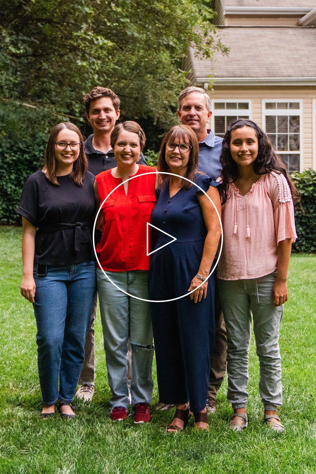 A family stands together on their lawn smiling at the camera with a play button overlayed