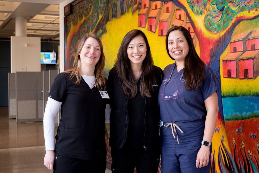 Behavioral therapist Tara Glavin, dentist Helen Mo, and dentist Jean Calvo stand in front of a colorful mural.